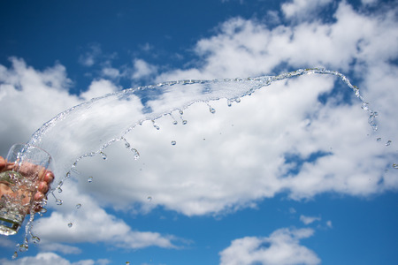 Splashing glass of  water against summer sky.の写真素材