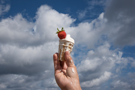 Hand holding melting ice cream against summer sky.の写真素材