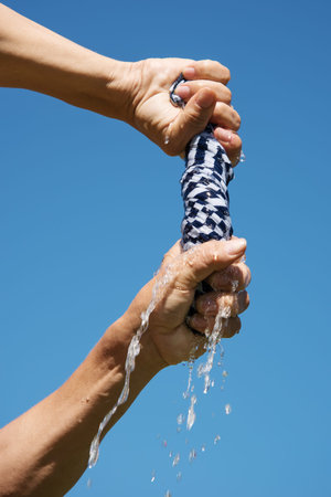 Hands squeeze wet fabric against blue sky.の写真素材