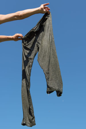 Hands holding wet trousers against blue sky.の写真素材