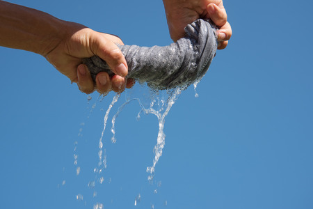 Hands squeeze wet fabric against blue sky.の写真素材