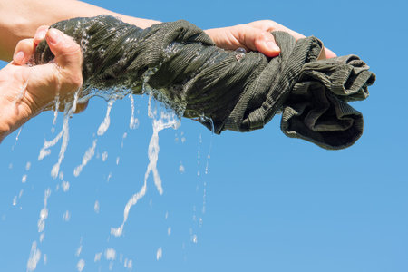Hands squeeze wet fabric against blue sky.
