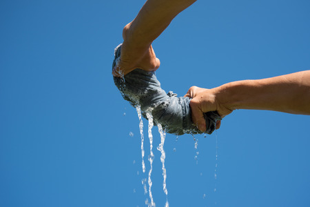 Hands squeeze wet cloth against blue sky.の写真素材