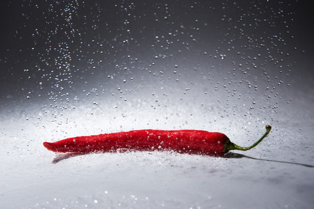 Flying water drops and red pepper.の写真素材