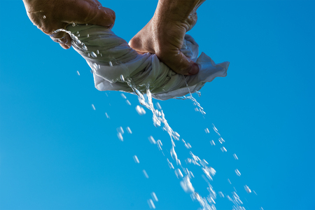 Squeezing of wet cloth against blue sky.の写真素材