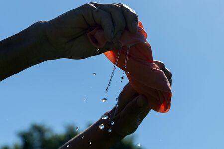 Hands twist pink cloth against blue sky.の写真素材
