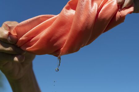 Hands twist pink cloth against blue sky.の写真素材