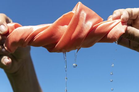 Hands twist pink cloth against blue sky.の写真素材