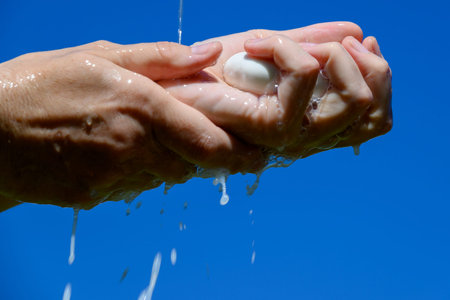 Washing hands by soap against blue sky.