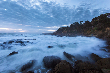 Dramatic ocean tide splashing water by rocky shore during sunset in Californiaの写真素材