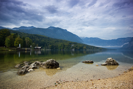 Cold mountain lake with a stones in front and fog above during cloudy sky, Bohijn Lake, Sloveniaの写真素材