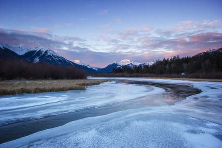 Cold calm river flowing through frozen valley from high mountains during sunrise, Vermilion lakes, Banff national park, Canadaの写真素材