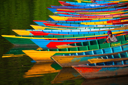 POKHARA, NEPAL - APRIL 13, 2012: Colorful moorage. Bright and colorful boats standing in one row on the water. A boatman (young Nepali boy) is sitting in one of them in Pokhara, Nepal.のeditorial素材