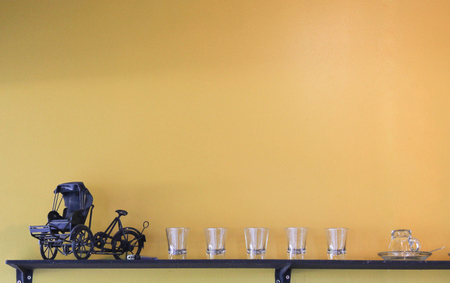Ancient tricycle, many thumbtack glasses and a cup on wooden wall shelves.の写真素材