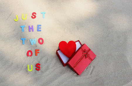 The words Just the two of us on sand with red heart in a red gift box.