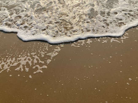 The waves on the sandy beach and white foam with the sunshine in summer morning.の写真素材