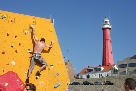 SCHEVENINGEN, HOLLAND - AUGUST 30, 2008: Annual Bouldering Competition on Scheveningen beach. Participant climbing artificial rock face with backdrop of Scheveningen lighthouseのeditorial素材
