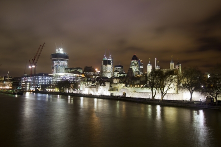 The illuminated Tower of London and modern office buildings with lighted windows at dusk in London, UKのeditorial素材