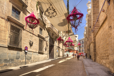 Toledo, Spain - June 1, 2016: Tourists walk in a decorated street beneath the cathedral during the Corpus Christi festival in Toledo, Spain on June 1, 2016のeditorial素材