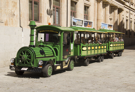 Salamanca, Spain - June 2, 2016: Little green tourist train with tourists drives past the historical buildings and shops in Calle Rua Mayor street in the old center of Salamanca, Spain on June 2, 2016のeditorial素材
