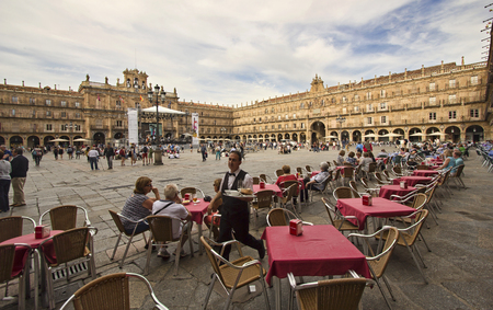 Salamanca, Spain - June 2, 2016: Waiter and other people walk on the historical Plaza Mayor,or main square, with tables and chairs of a restaurant in the old center of Salamanca, Spain on June 2, 2016のeditorial素材