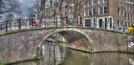 Canal and bridge in historical Amsterdam, Holland, with parked bicycles and cars and trees in winterのeditorial素材