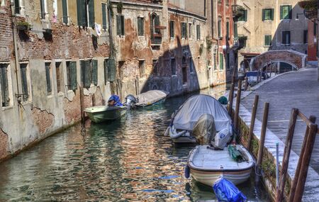 Historical buildings and small bridge across a canal with boats in Venice, Italyの写真素材