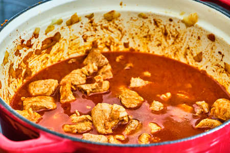 Preparing perkelt sauce - cooking meat, dried pepper, liquid and onion in red potの写真素材