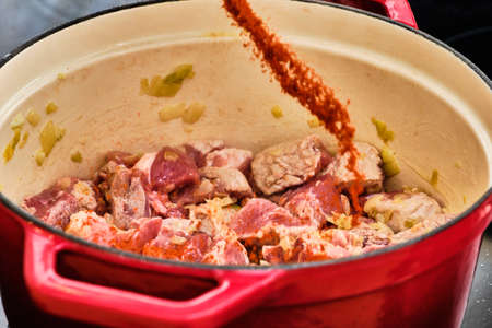 Preparing perkelt sauce - pouring dried pepper on meat in red potの写真素材