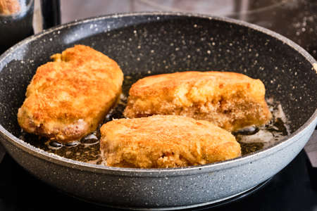 Cooking tasty stuffed schnitzel with ham and cheese on frying panの写真素材