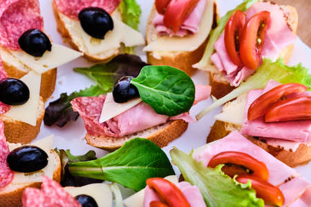Tasty small sandwiches with ham and salami and vegetables on white plateの写真素材