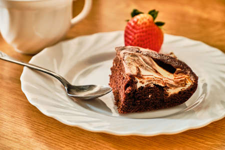 Tasty homemade cocoa cake with curd and strawberry on white plate with teaspoon and cup of hot drinkの写真素材