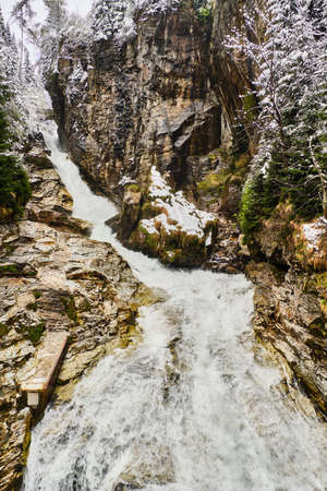 Waterfall stream on rocks by trees covered by melting snow in spring in Bad Gasterの写真素材