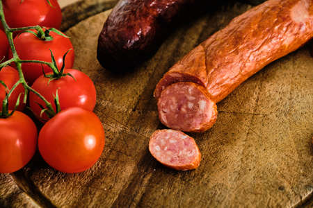 Tasty sliced sausage on wooden cutting board with red tomatoの写真素材