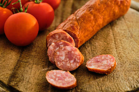Tasty sliced sausage on wooden cutting board with red tomatoの写真素材