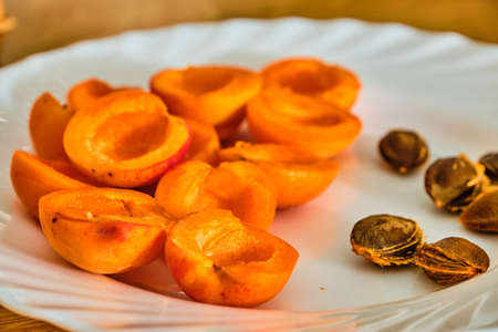 Tasty fresh apricot fruit sliced on half and stones on wihte plate on wooden tableの写真素材