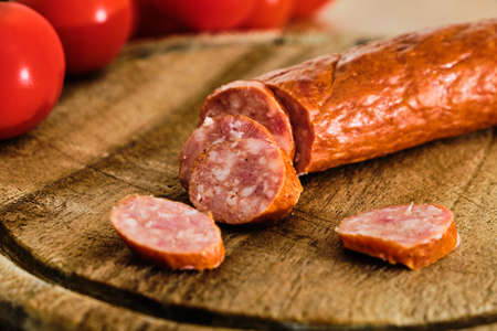 Tasty sliced sausage on wooden cutting board with red tomatoの写真素材