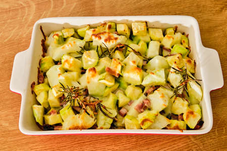 Gratin pattypan squash and zucchini with cheese, ham and rosemary herb in red bowl preparingの写真素材