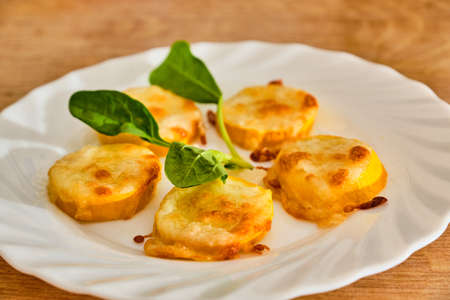 Baked tasty and fresh yellow zucchini with mozzarella and parmesan cheese on white plate with green plant. On wooden table.の写真素材