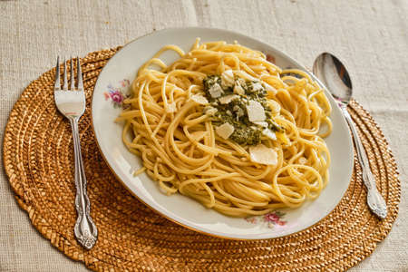 Tasty fresh spaghetti with basil pesto sauce and parmesan on white plate with serving on table with clothの写真素材