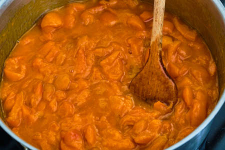 Cooking apricots in pot with wooden spoon preparing homemade marmeladeの写真素材