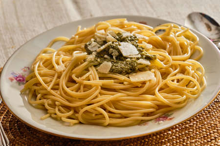 Tasty fresh spaghetti with basil pesto sauce and parmesan on white plate with serving on table with clothの写真素材