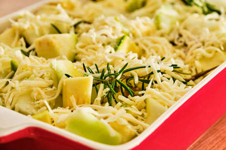 Fresh pattypan squash and zucchini with cheese, ham and rosemary herb in red bowl preparing gratin vegetableの写真素材