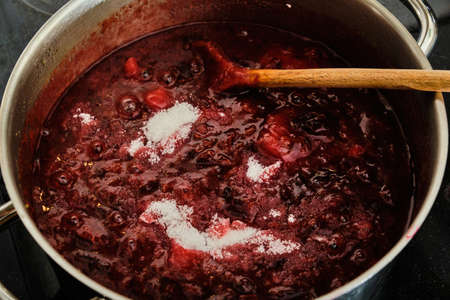 Stiring sugar in boiling plum fruit preparing tasty homemade marmalade close up detailの写真素材
