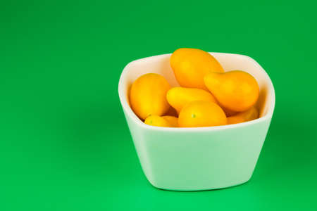 Fresh and tasty yellow tomatoes in white bowl isolated on green backgroundの写真素材