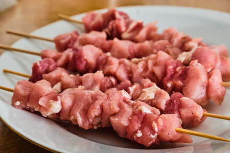 Raw pork meat souvlaki on white plate on wooden tableの写真素材
