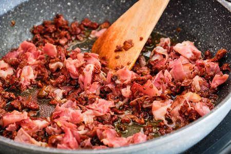 Cooking tasty mixture for spaghetti - dried tomatoes and dried ham on frying pan preparing with wooden spatulaの写真素材