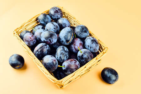 Tasty and fresh violet plum fruit in basket isolated on beige backgroundの写真素材