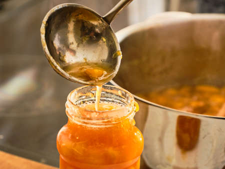 Pouring prepared homemade peach marmalade in glass by mettal ladle in kitchenの写真素材