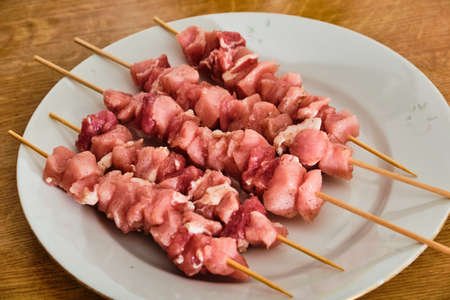 Raw pork meat souvlaki on white plate on wooden tableの写真素材